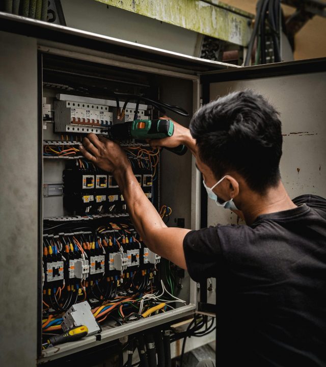 Technician working on circuit breaker panel, adjusting electrical wires indoors.